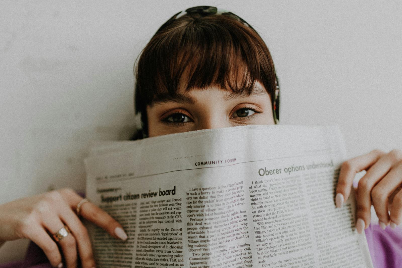 Young woman with a newspaper, focused on half-revealed eyes. Studio portrait.