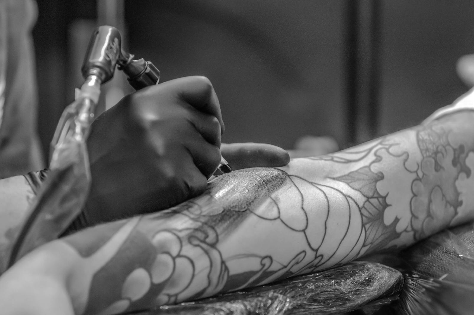 Artistic black and white photo capturing the detailed process of tattooing an arm.